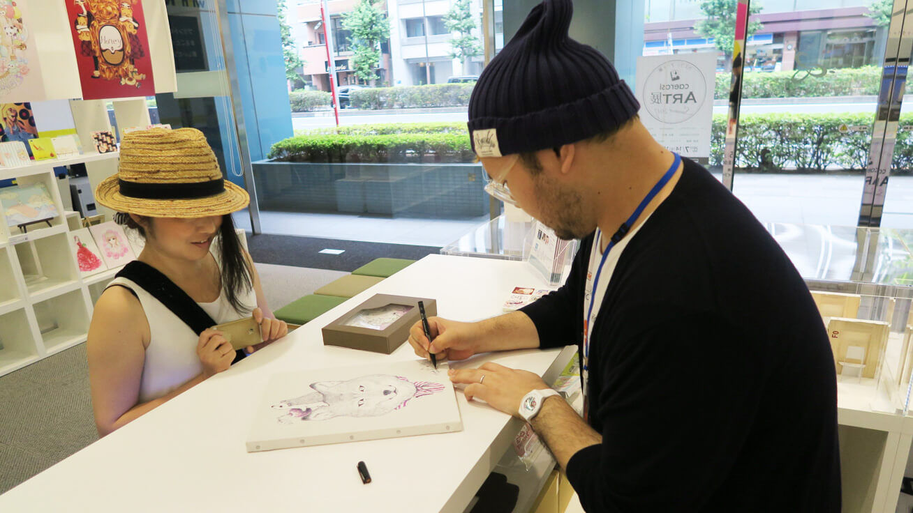 UVプリンターで製作した作品にサインをし、お客様にお渡しするいわさきゆうしさん